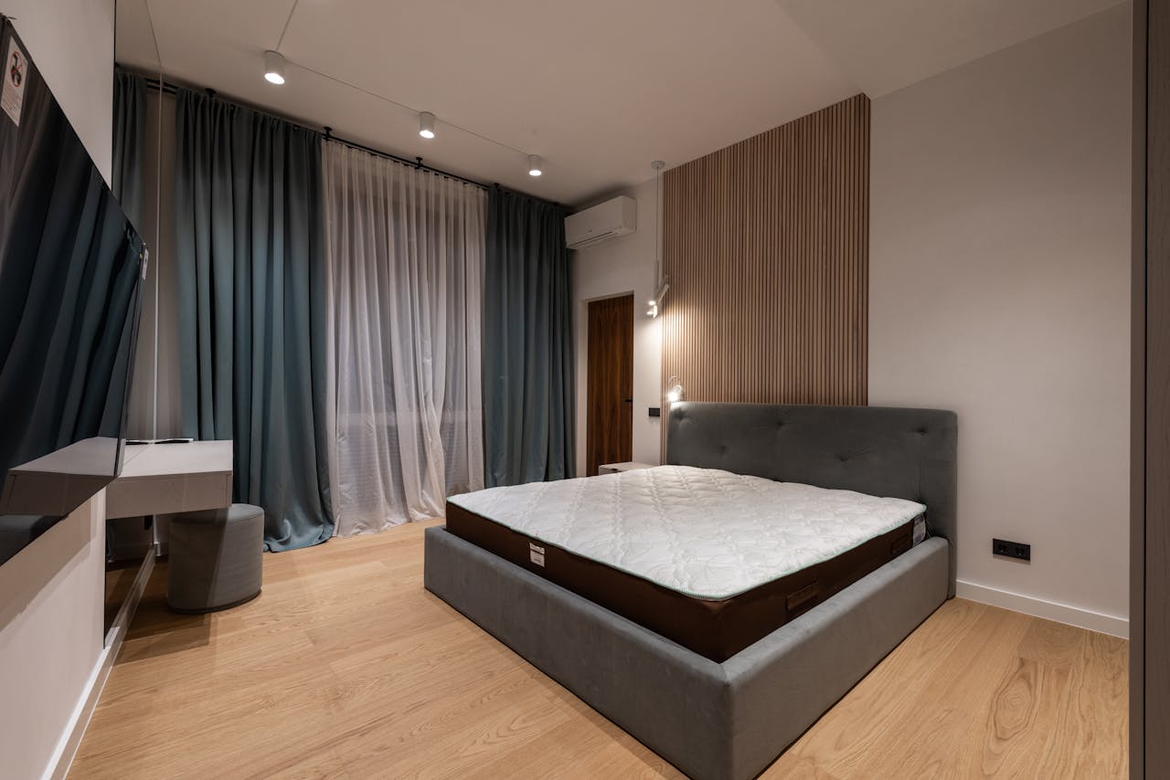 Modern TV set and comfy bed in stylish room decorated with lamps and curtains